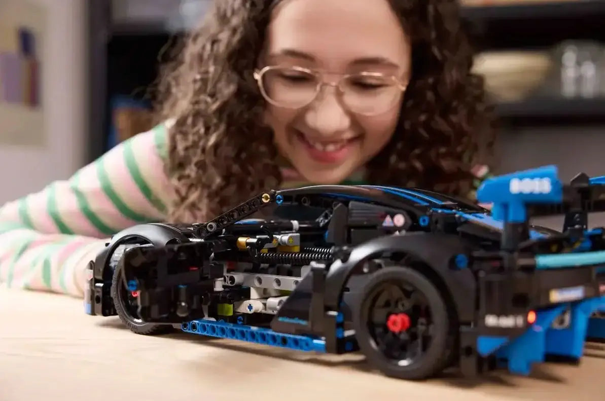 Dziewczynka z kręconymi włosami bawi się kreatywną zabawką samochodem LEGO na stole - zabawki-dla-dziewczynki