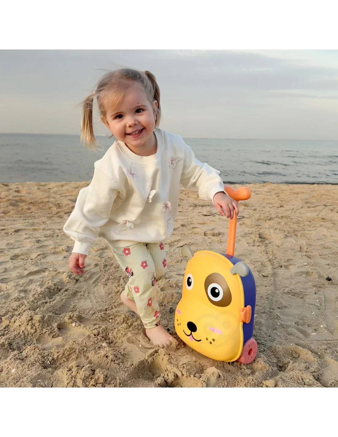 Uśmiechnięta dziewczynka z walizką w kształcie psa na plaży, zabawki dla dziewczynki zabawki-dla-dziewczynki