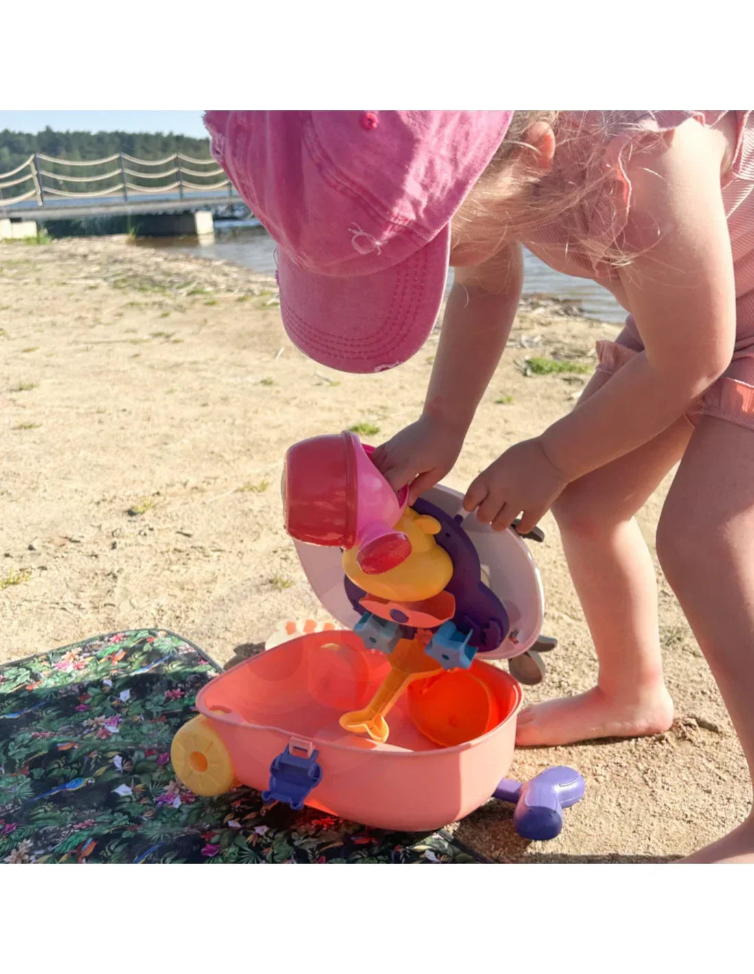 Dziewczynka w różowej czapce bawi się kolorową zabawką na plaży  - zabawki-dla-dziewczynki