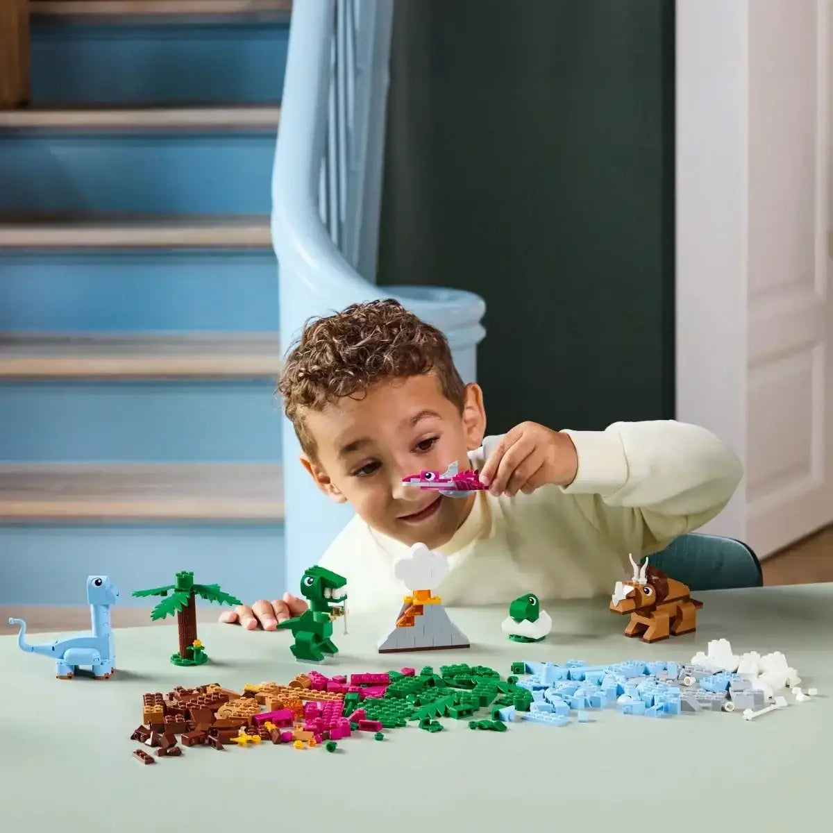 Chłopiec bawiący się klockami LEGO dinozaury przy stole, zabawki kreatywne dla dzieci  - zabawki-dla-dziewczynki