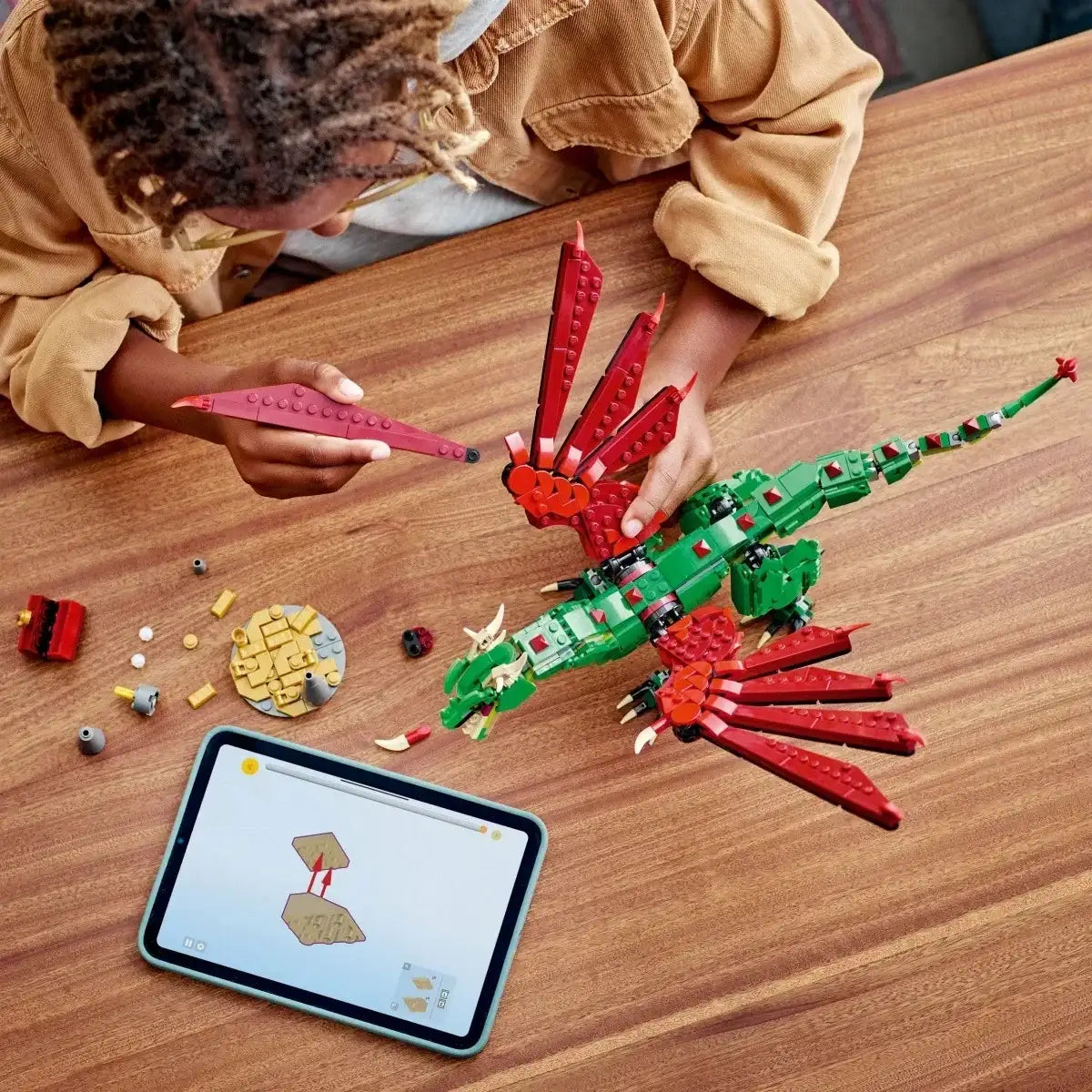 Dziecko składa zielonego smoka z klocków LEGO, obok tablet z instrukcją, kreatywna zabawka dla dziewczynki - zabawki-dla-dziewczynki